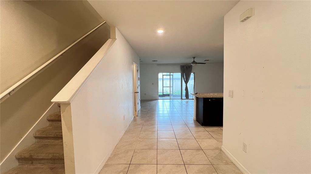 A carpeted staircase leads to an open-concept living area with tile flooring and sliding doors — 9017 ALBA LANE, KISSIMMEE, FL