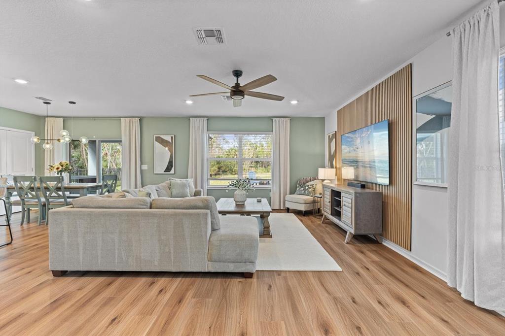 A living room features light green walls, wood-look flooring, a slatted wood accent wall, and furniture — 11875 ARMADA WAY, PARRISH, FL