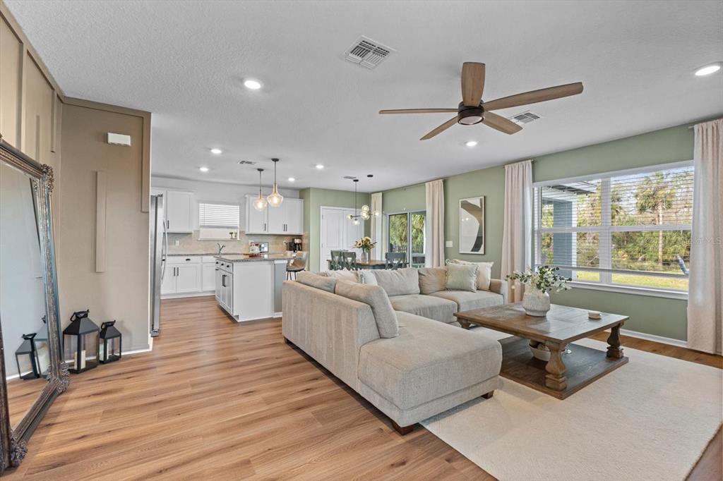An open-concept living room and kitchen featuring light wood flooring, a sectional sofa, and windows — 11875 ARMADA WAY, PARRISH, FL
