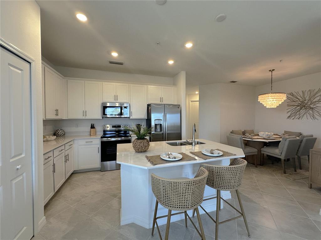 A modern kitchen features white cabinets, stainless steel appliances, a central island, and tile flooring — 14201 HERITAGE LANDING BOULEVARD UNIT 1338, PUNTA GORDA, FL