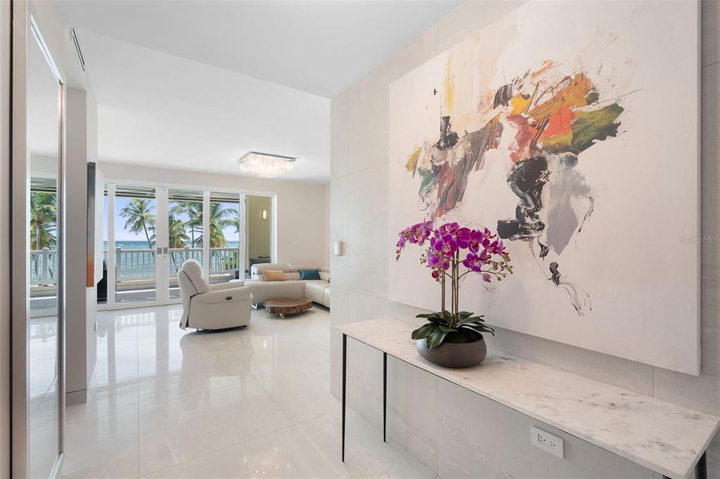A bright hallway with a marble console table and abstract art leads to a living area — 400 OCEAN DRIVE UNIT 423, HUMACAO, PR