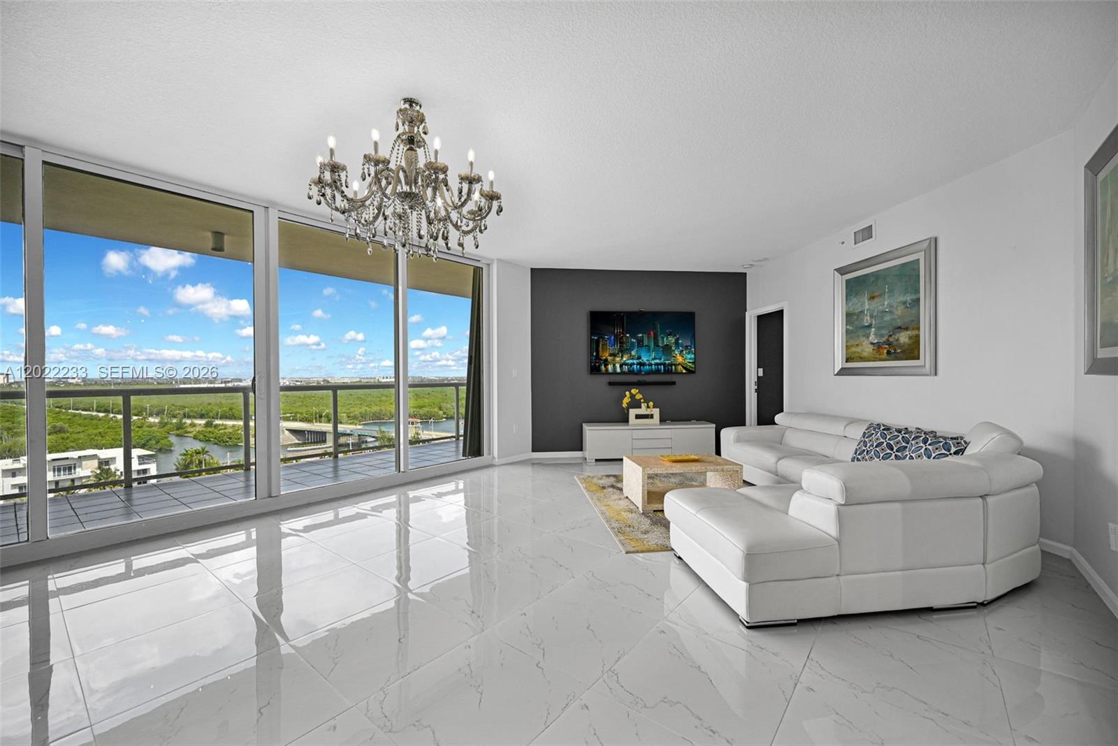 A modern living room features white tile floors, a crystal chandelier, and a balcony view — 6001 N Ocean Dr # 1203, Hollywood FL 33019, HOLLYWOOD, FL
