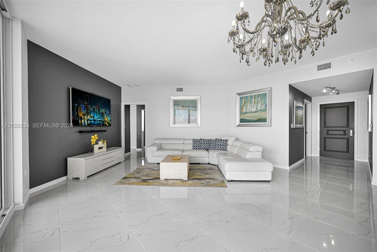 A living room features a white sectional sofa, a dark accent wall, and a crystal chandelier — 6001 N Ocean Dr # 1203, Hollywood FL 33019, HOLLYWOOD, FL