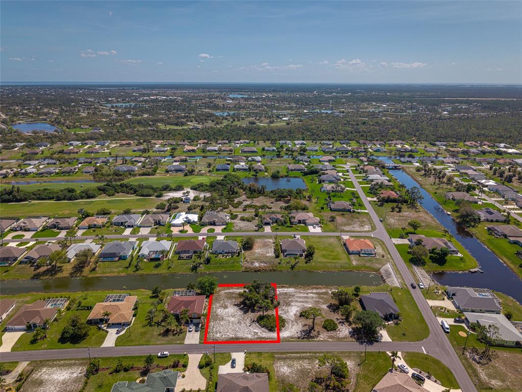 An aerial view shows a vacant residential lot outlined in red next to a canal — 47 MEDALIST LANE, ROTONDA WEST, FL