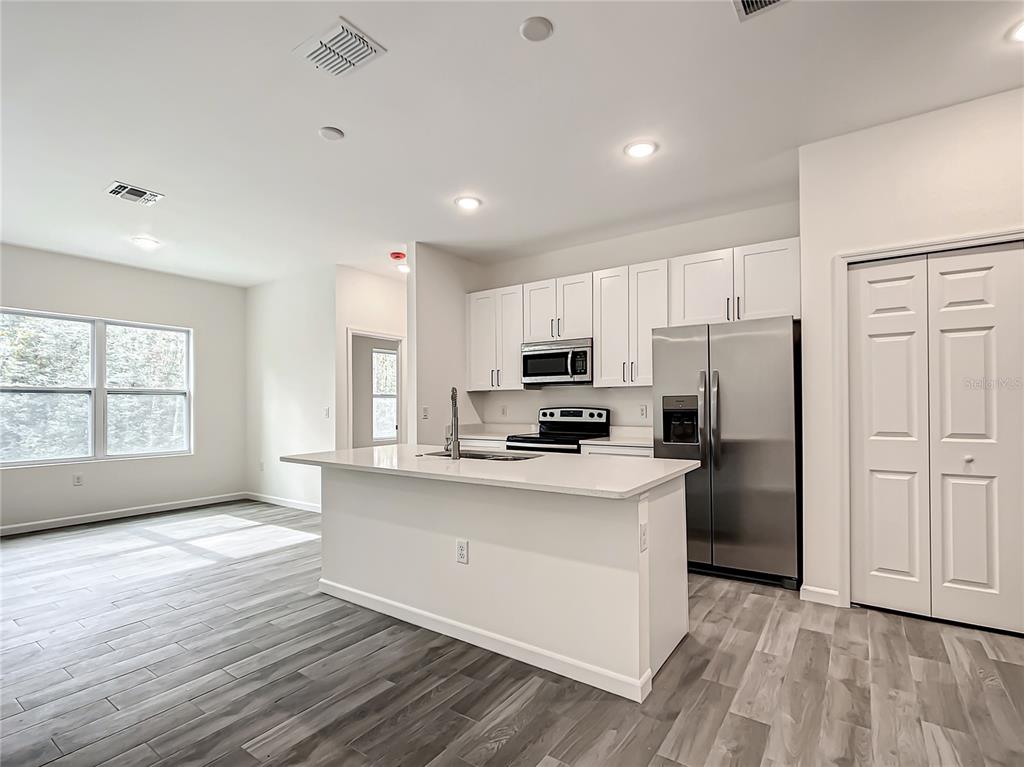 A kitchen features white cabinets, stainless steel appliances, a center island, and wood-look flooring — 8070 SW 131ST LANE, OCALA, FL