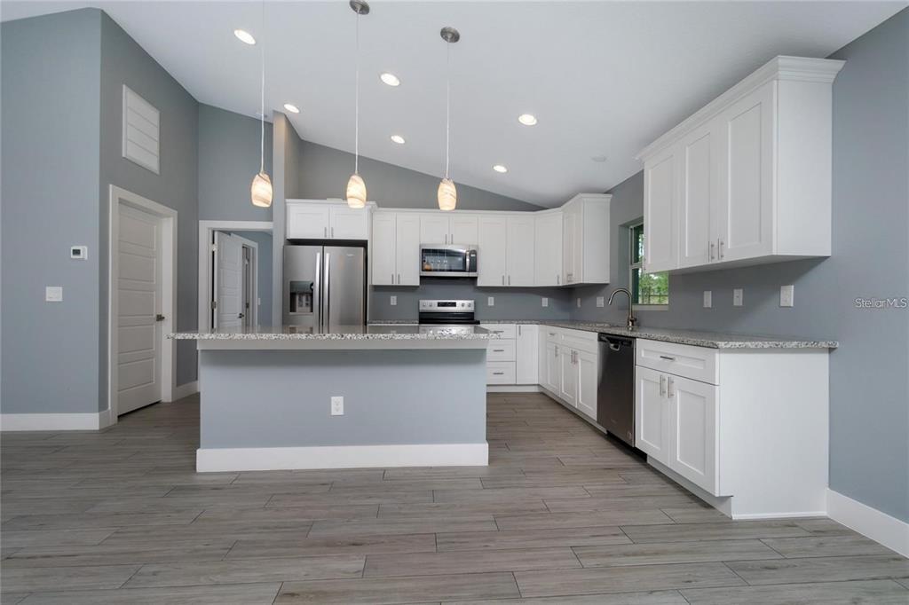A kitchen with white cabinets, granite countertops, stainless steel appliances, and gray wood-look flooring — 0 LONGFELLOW LANE, NORTH PORT, FL
