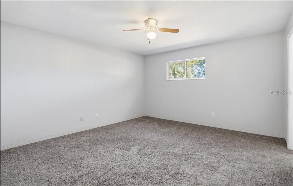 An empty bedroom with gray carpet, white walls, a ceiling fan, and a single window — 5991 FAIRFIELD AVENUE S, GULFPORT, FL
