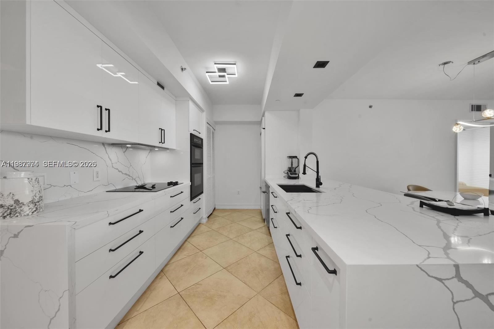 A modern kitchen features white cabinetry, marble-patterned countertops, and black hardware on a tiled floor — 1830 S Ocean Dr # 4704, Hallandale Beach FL 33009, HALLANDALE BEACH, FL