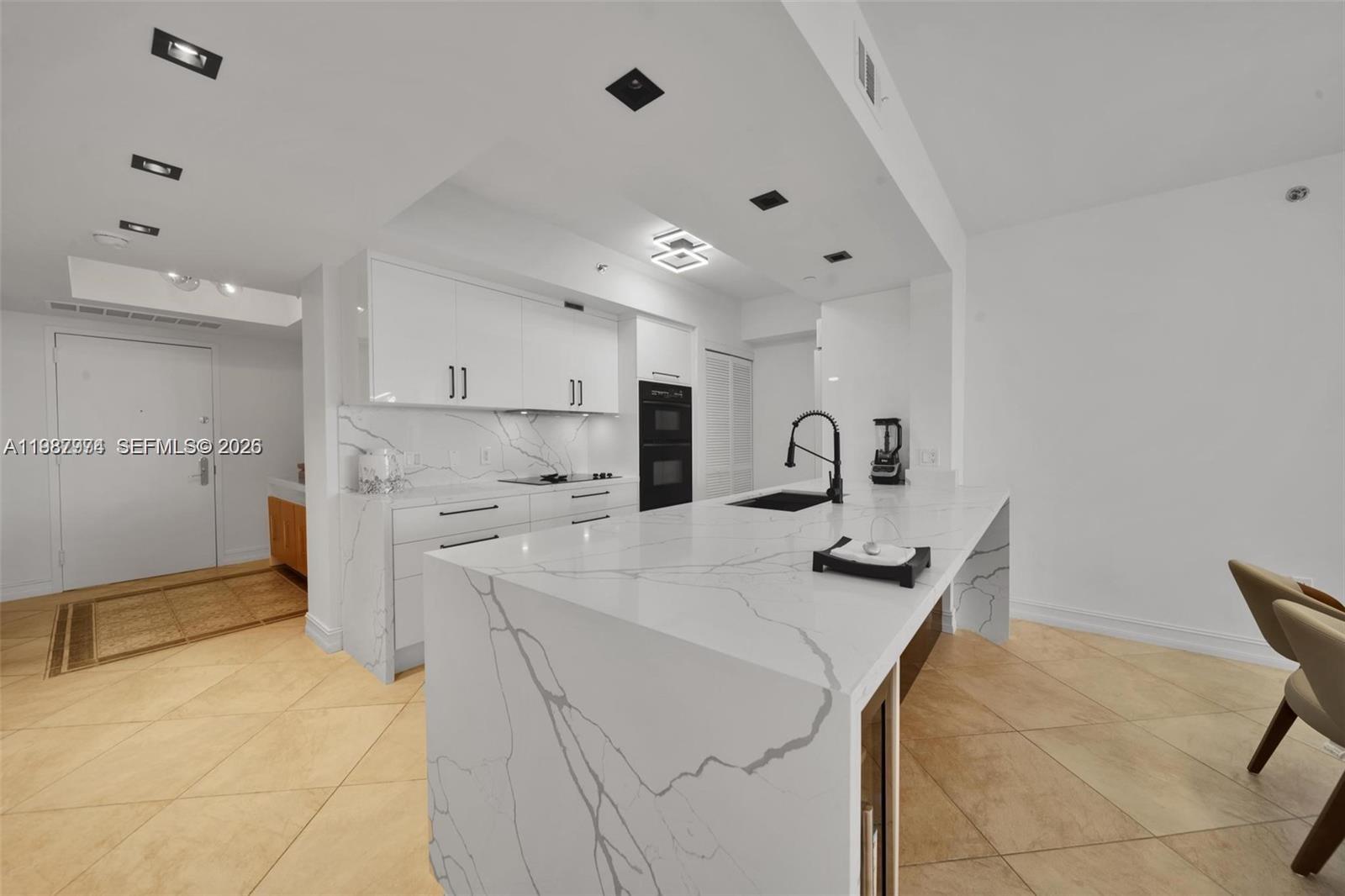 A modern kitchen features a large marble-topped island, white cabinetry, and light-colored tile flooring — 1830 S Ocean Dr # 4704, Hallandale Beach FL 33009, HALLANDALE BEACH, FL