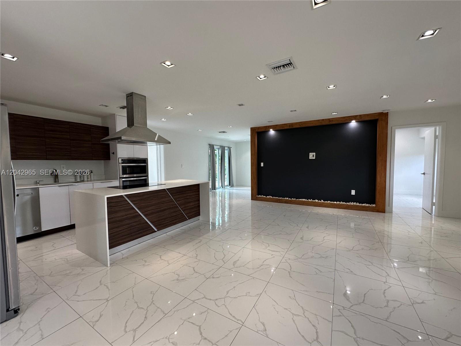 A modern kitchen features a white island with wood accents, marble-look tile floors, and a black accent wall — 10010 SW 162nd St, Miami FL 33157, MIAMI, FL