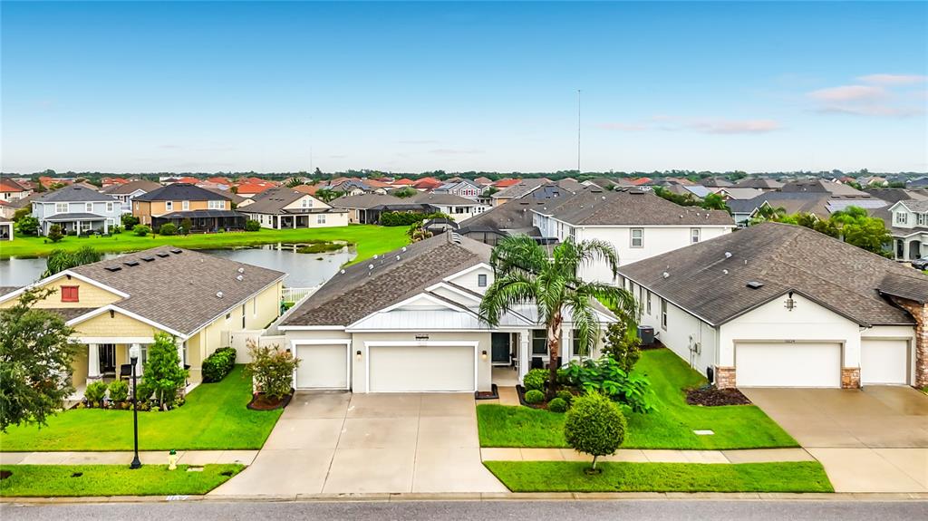 An aerial view shows three suburban houses with attached garages and manicured lawns near a pond — 13222 MOSS GRASS WAY, RIVERVIEW, FL