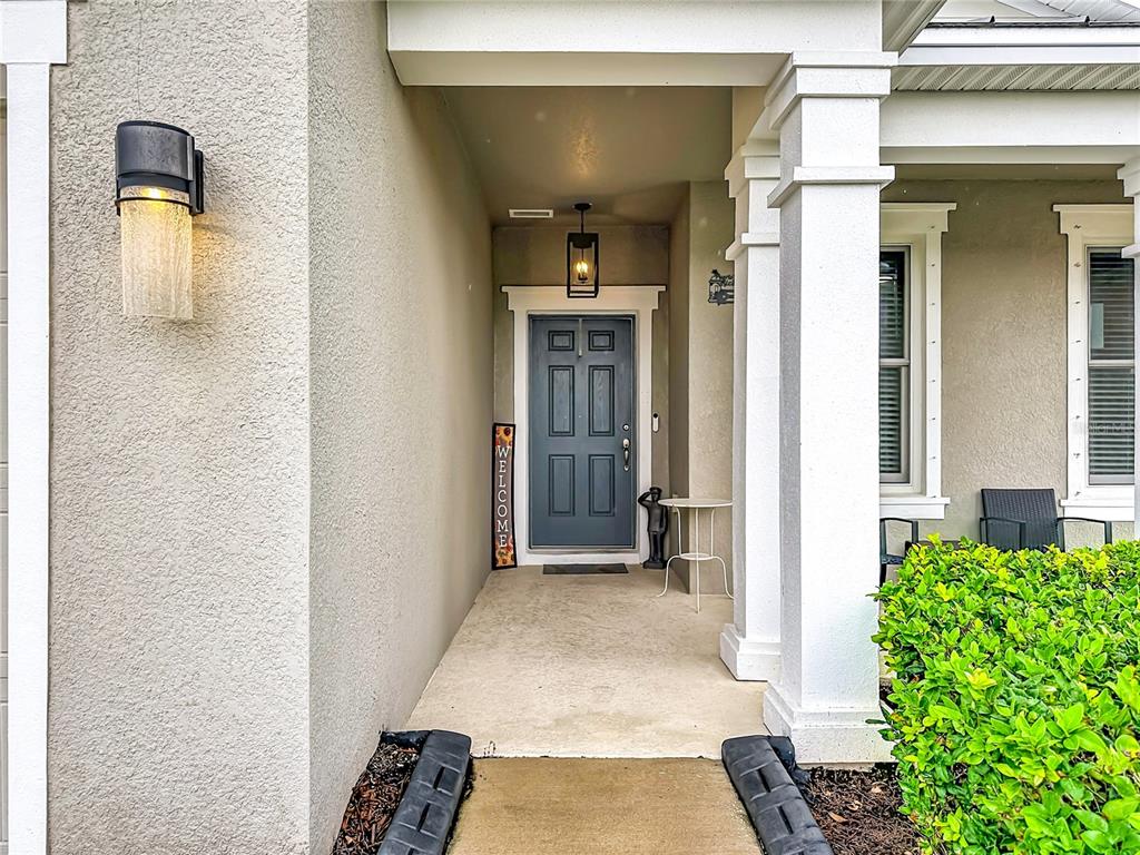 A covered front porch features a blue door, a welcome sign, and two outdoor lights — 13222 MOSS GRASS WAY, RIVERVIEW, FL