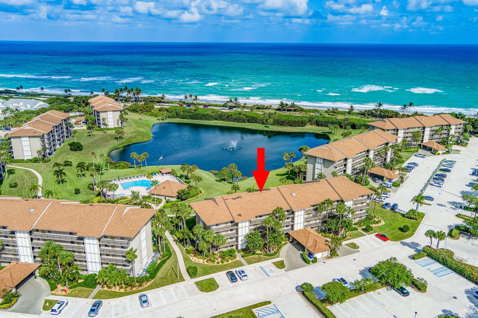 An aerial view shows a multi-story apartment complex with a lake, pool, and oceanfront — 501 S Seas Drive # 202, Jupiter FL 33477, JUPITER, FL