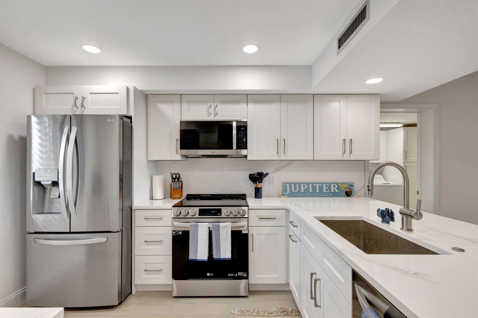 A modern kitchen features white cabinets, stainless steel appliances, and white quartz countertops — 501 S Seas Drive # 202, Jupiter FL 33477, JUPITER, FL