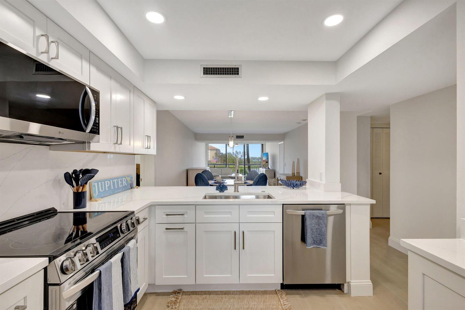 A modern kitchen features white cabinets, stainless steel appliances, and a view into the dining area — 501 S Seas Drive # 202, Jupiter FL 33477, JUPITER, FL