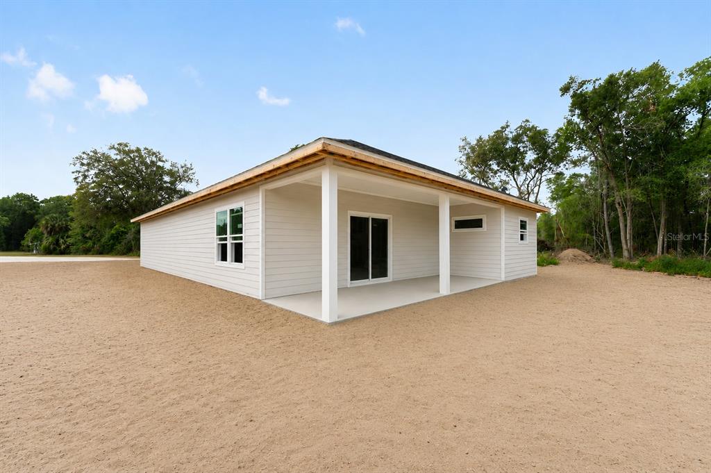 A light-colored house exterior features a covered patio, sliding glass doors, and unfinished roof eaves — 13291 NE 54TH STREET, WILLISTON, FL