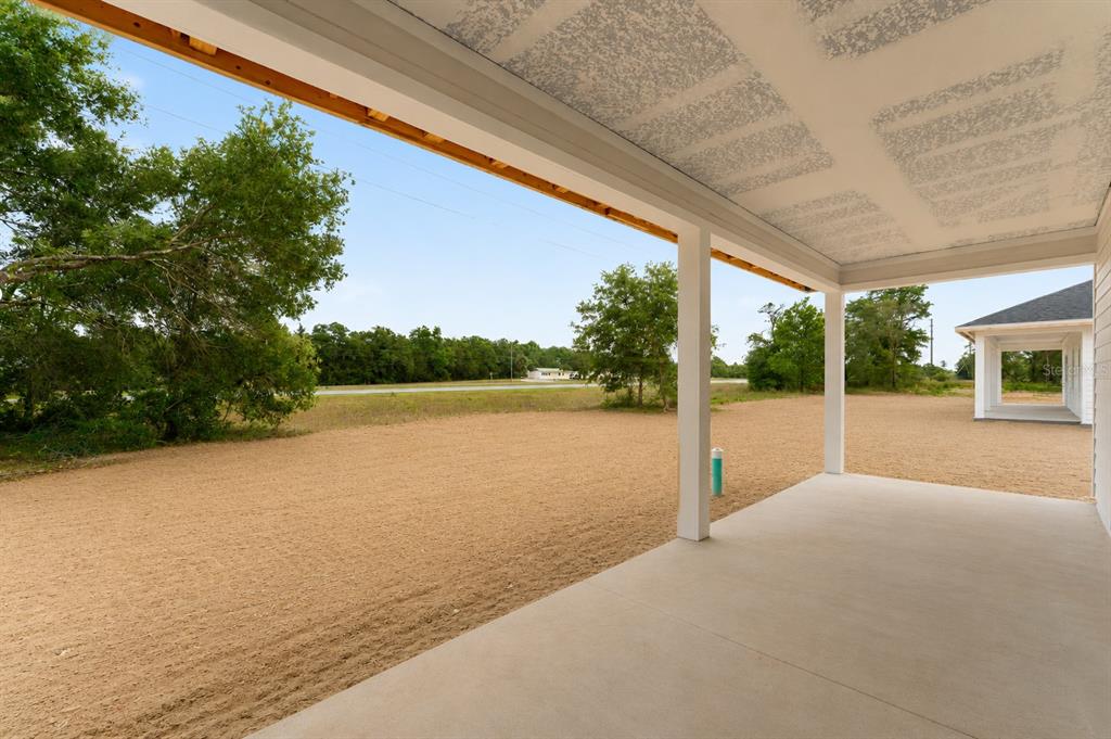 A covered concrete patio overlooks a large, sandy yard with trees and a distant road — 13291 NE 54TH STREET, WILLISTON, FL