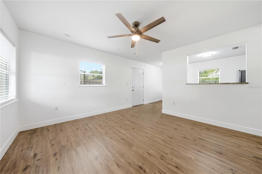 A bright living room features wood-look flooring, a ceiling fan, and a kitchen pass-through window — 1009 NEBRASKA STREET, LEESBURG, FL