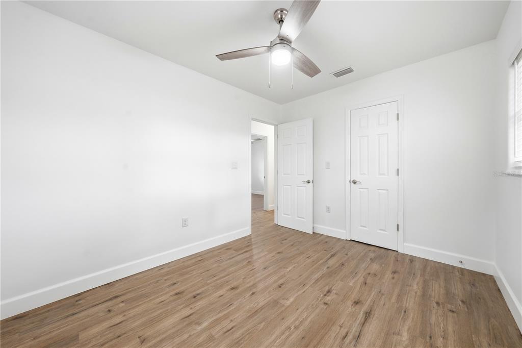 An empty bedroom with white walls, wood-look flooring, a ceiling fan, and two white doors — 1009 NEBRASKA STREET, LEESBURG, FL