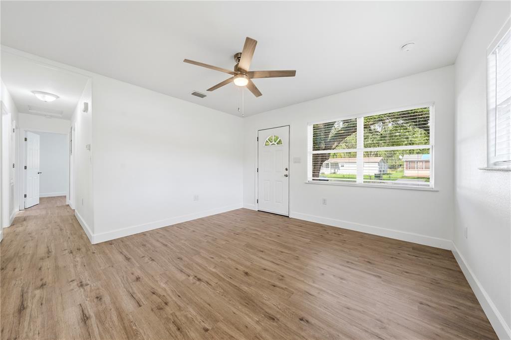 A bright room with wood-look flooring, a ceiling fan, a white door, and large windows — 1009 NEBRASKA STREET, LEESBURG, FL