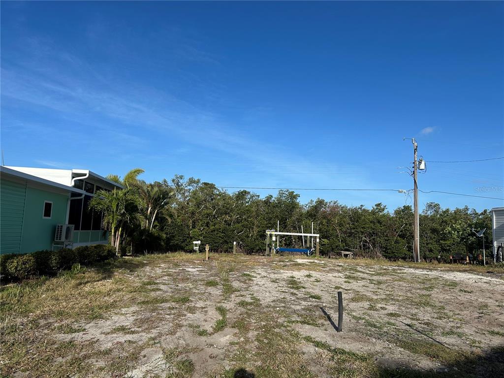 A vacant, sandy lot sits next to a house with a blue exterior — 196 BIMINI DRIVE, PALMETTO, FL