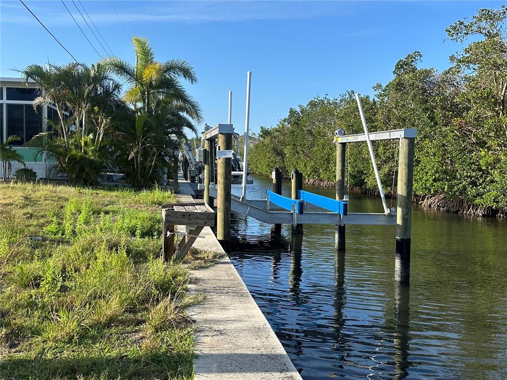 A boat lift sits in a canal next to a concrete seawall and palm trees — 196 BIMINI DRIVE, PALMETTO, FL