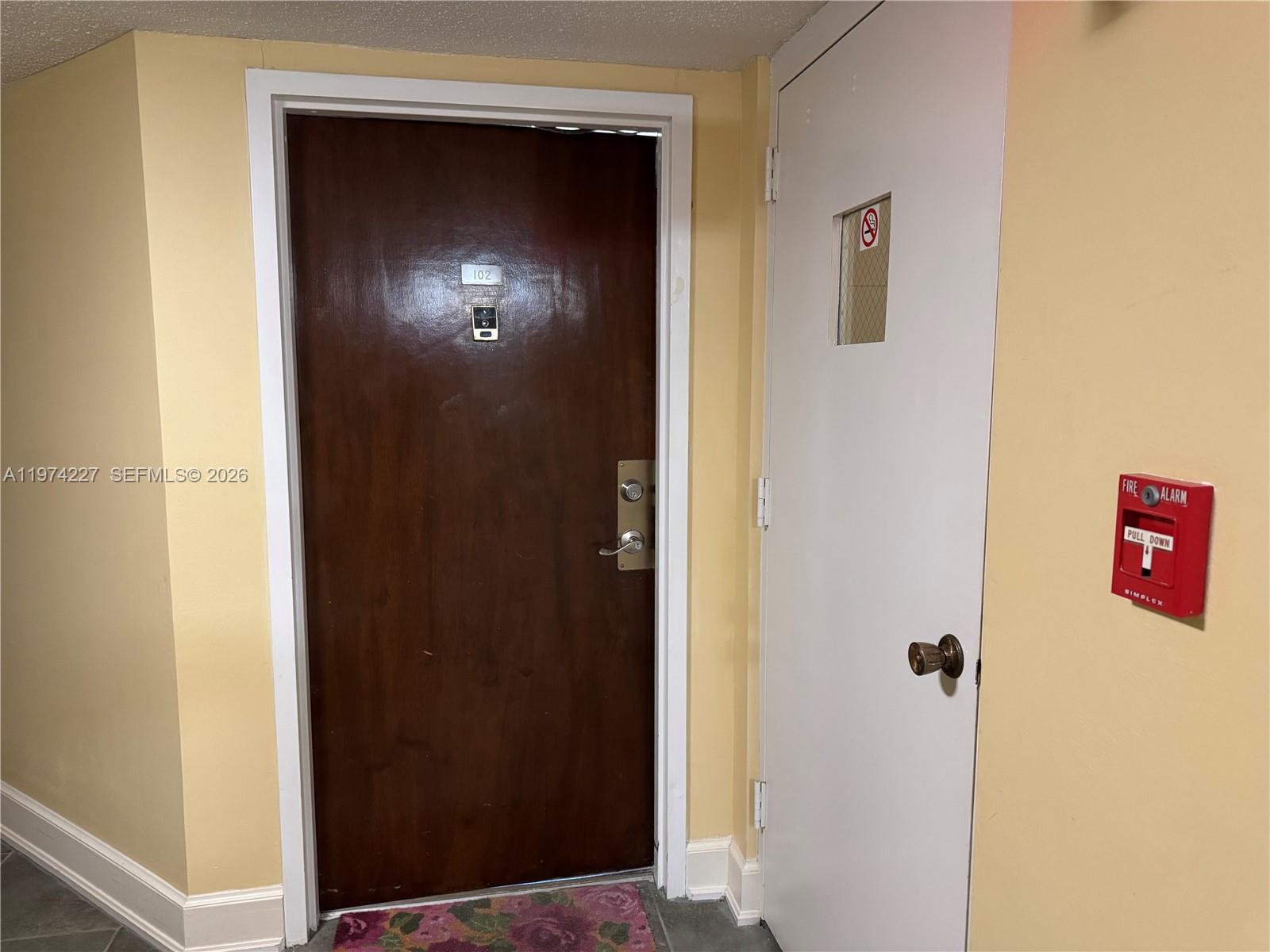 A brown apartment door labeled 102 sits next to a white door with a fire alarm — 925 N Halifax # 102, Daytona FL 32118, DAYTONA, FL