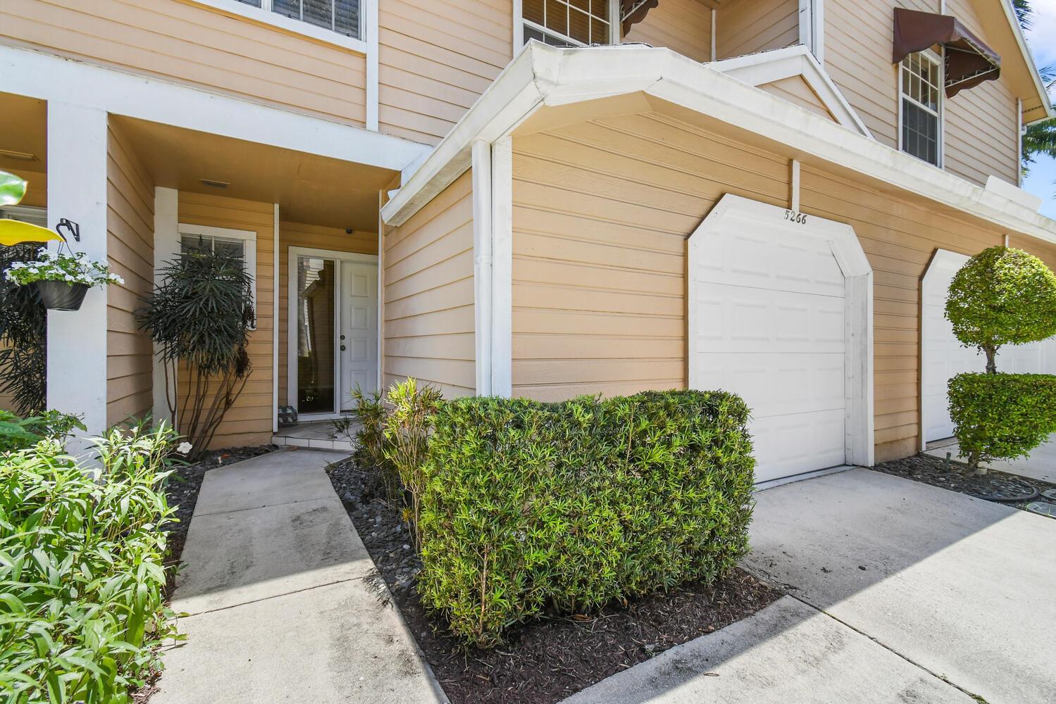 An exterior view of a tan two-story townhouse with a garage and front walkway — 5266 Sapphire Valley, Boca Raton FL 33486, BOCA RATON, FL