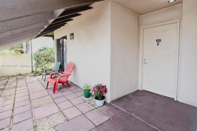 A covered patio features a red chair, a green chair, potted plants, and a door — 101 SW 96th Ter # 101, Plantation FL 33324, PLANTATION, FL