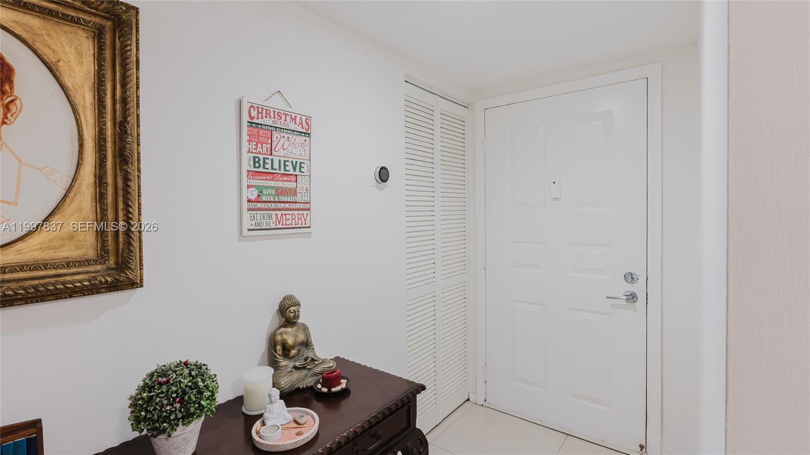 An entryway features a white door, a louvered closet, a Buddha statue, and wall decor — 101 SW 96th Ter # 101, Plantation FL 33324, PLANTATION, FL
