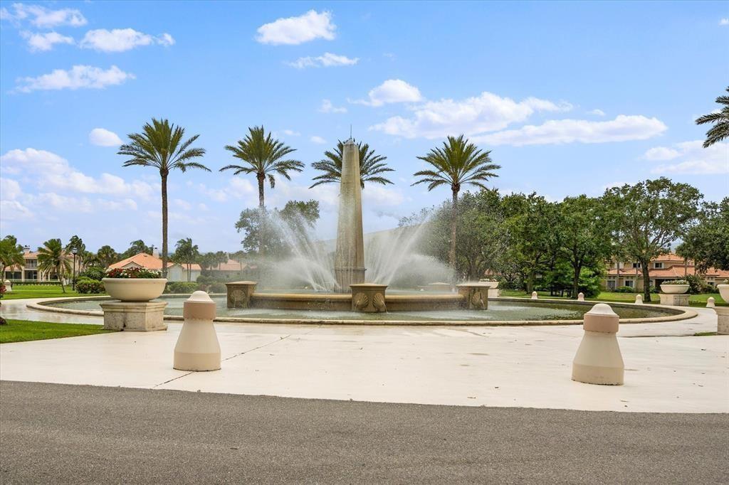 A large outdoor fountain with a central obelisk stands in a landscaped residential community — 5060 Harmony Circle # 104, Vero Beach FL 32967, VERO BEACH, FL