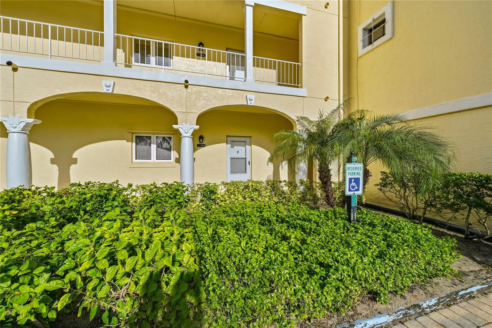 A yellow building exterior features a ground-level patio, a balcony above, and a handicap sign — 5060 Harmony Circle # 104, Vero Beach FL 32967, VERO BEACH, FL