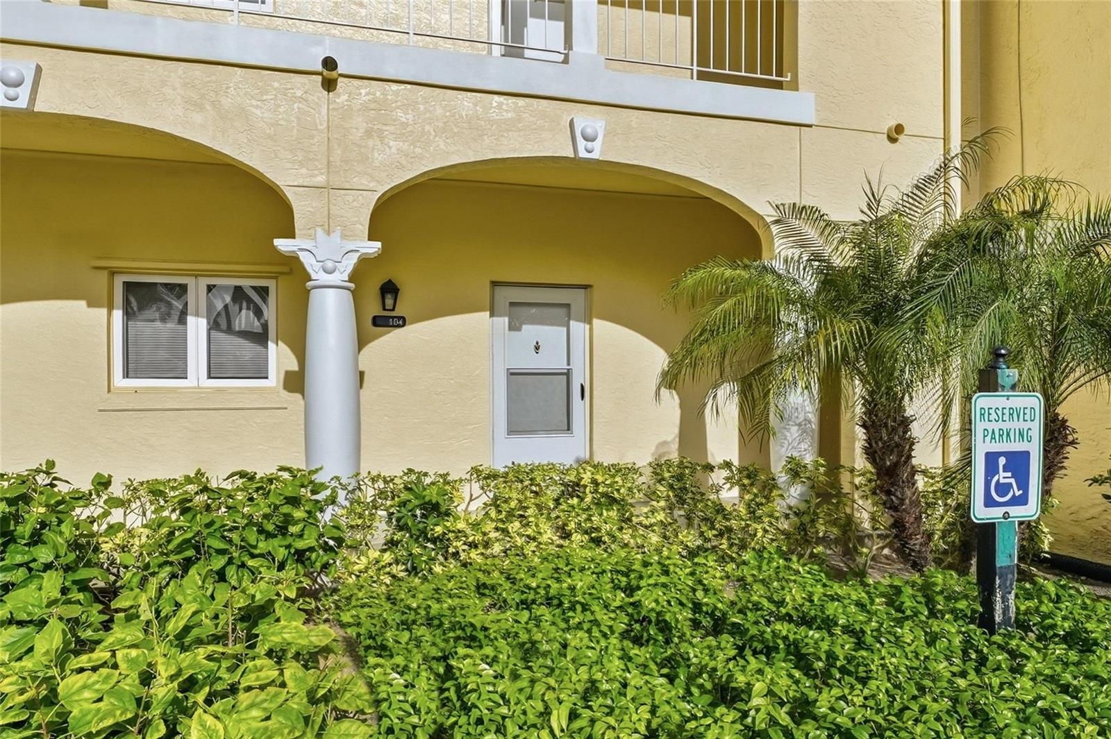 A ground-floor apartment entrance with a white door, arched porch, and a handicap parking sign — 5060 Harmony Circle # 104, Vero Beach FL 32967, VERO BEACH, FL