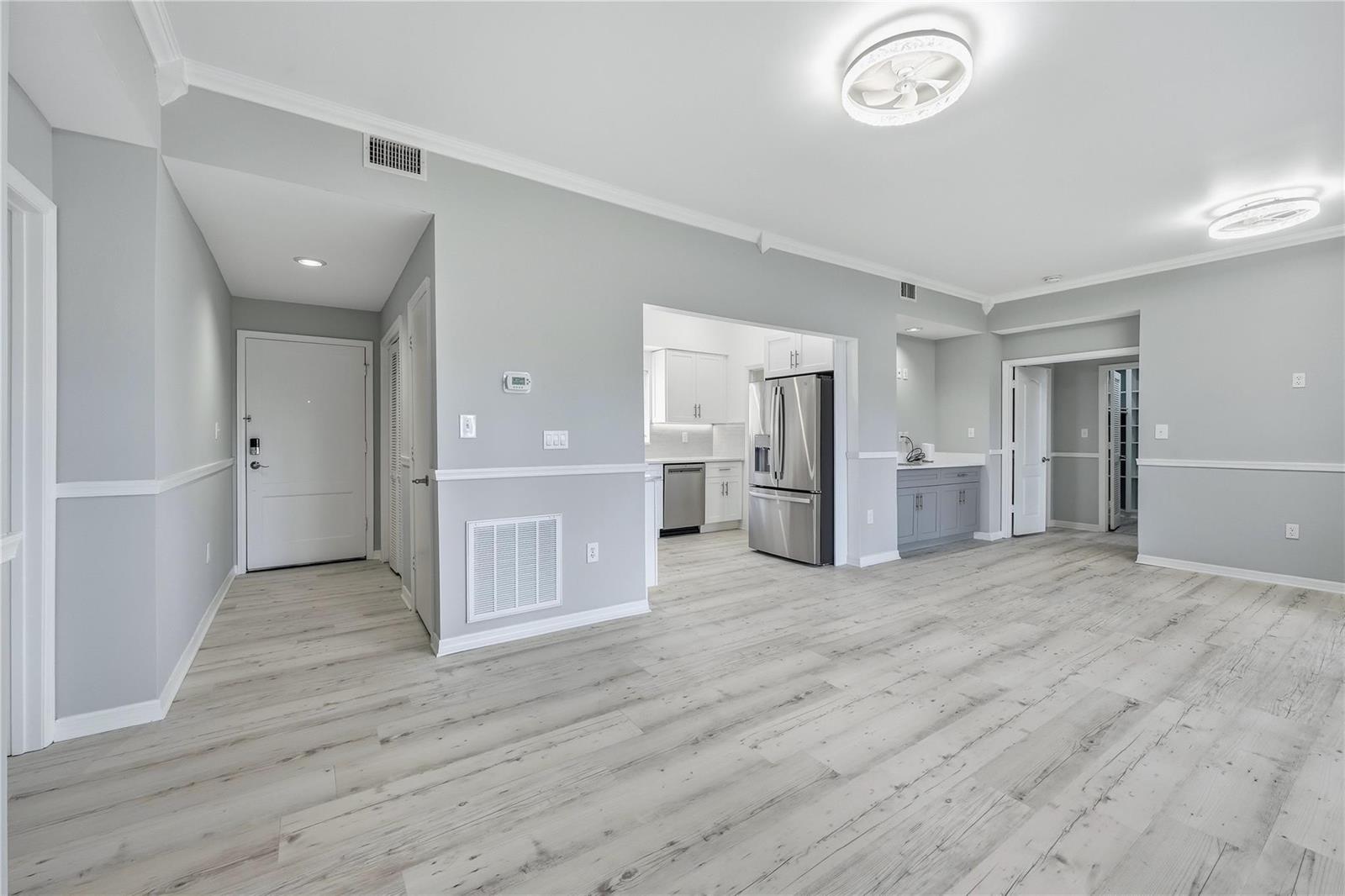 An open-concept living area features light gray walls, wood-look flooring, and a kitchen with stainless appliances — 5060 Harmony Circle # 104, Vero Beach FL 32967, VERO BEACH, FL