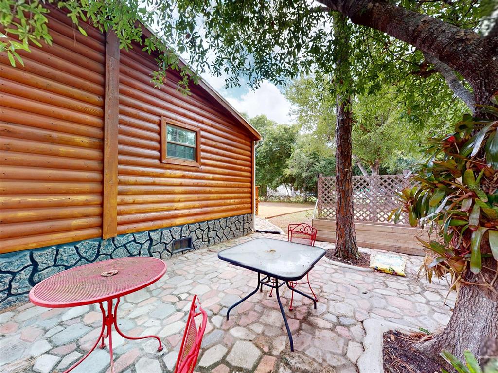 A stone patio with two tables and chairs sits beside a log cabin exterior — 17021 SHELBY LANE, NORTH FORT MYERS, FL