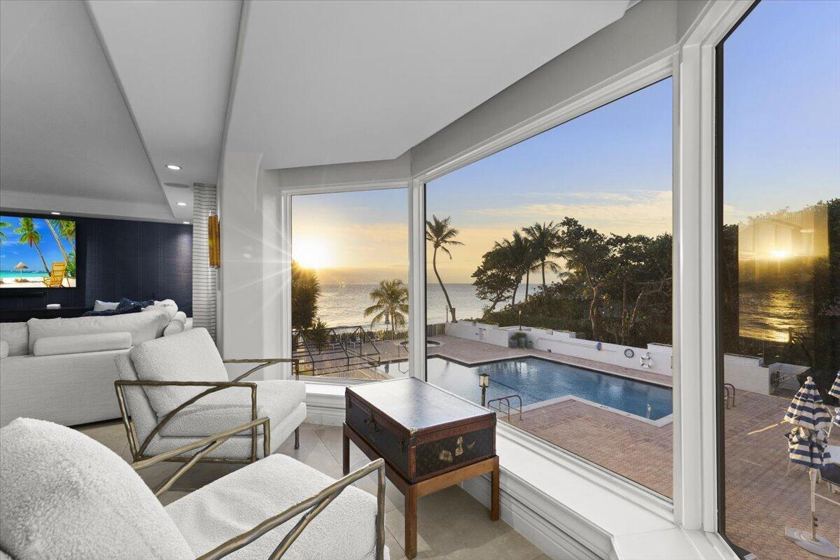 A living room with white armchairs overlooks a swimming pool and the ocean at sunset — 4605 S Ocean Boulevard # 3b, Highland Beach FL 33487, HIGHLAND BEACH, FL