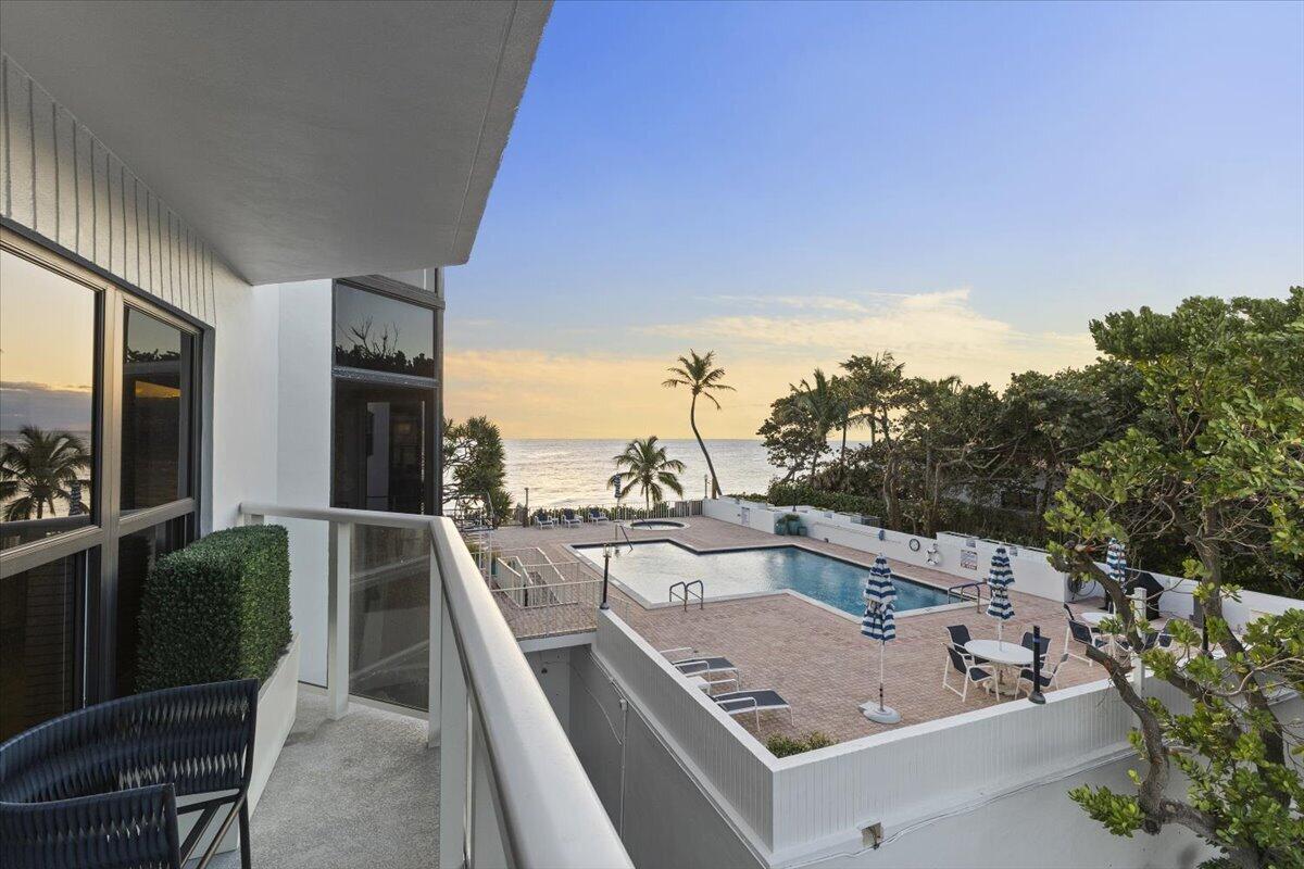 A balcony overlooks a swimming pool and patio area with an ocean view at sunset — 4605 S Ocean Boulevard # 3b, Highland Beach FL 33487, HIGHLAND BEACH, FL