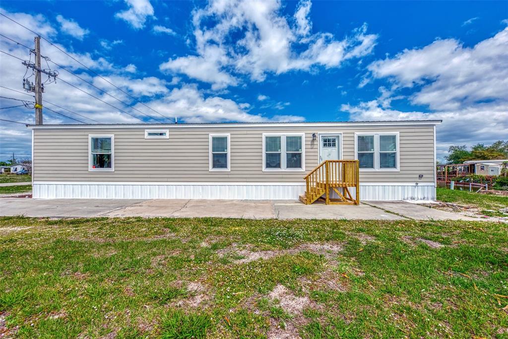 A single-story manufactured home with light gray siding, a concrete patio, and wooden front steps — 1391 FLAMINGO DRIVE, ENGLEWOOD, FL