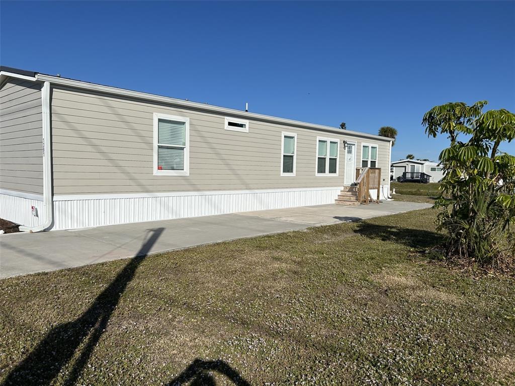 A light-colored manufactured home features horizontal siding, a concrete driveway, and a small wooden porch — 1391 FLAMINGO DRIVE, ENGLEWOOD, FL