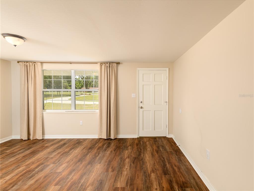 A room with wood-look flooring, a window with curtains, and a white entry door — 4722 STEARNS ROAD, VALRICO, FL