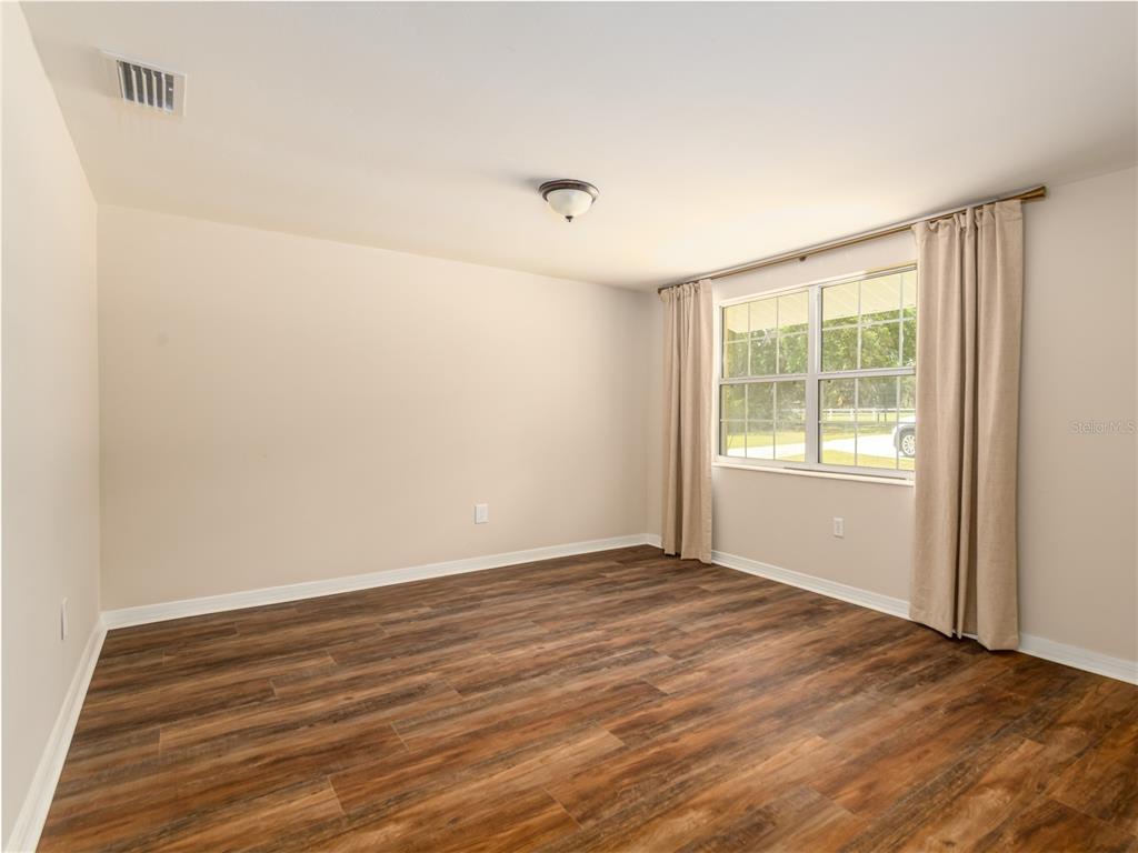 An empty room features light-colored walls, wood-look flooring, a ceiling light, and a window with curtains — 4722 STEARNS ROAD, VALRICO, FL
