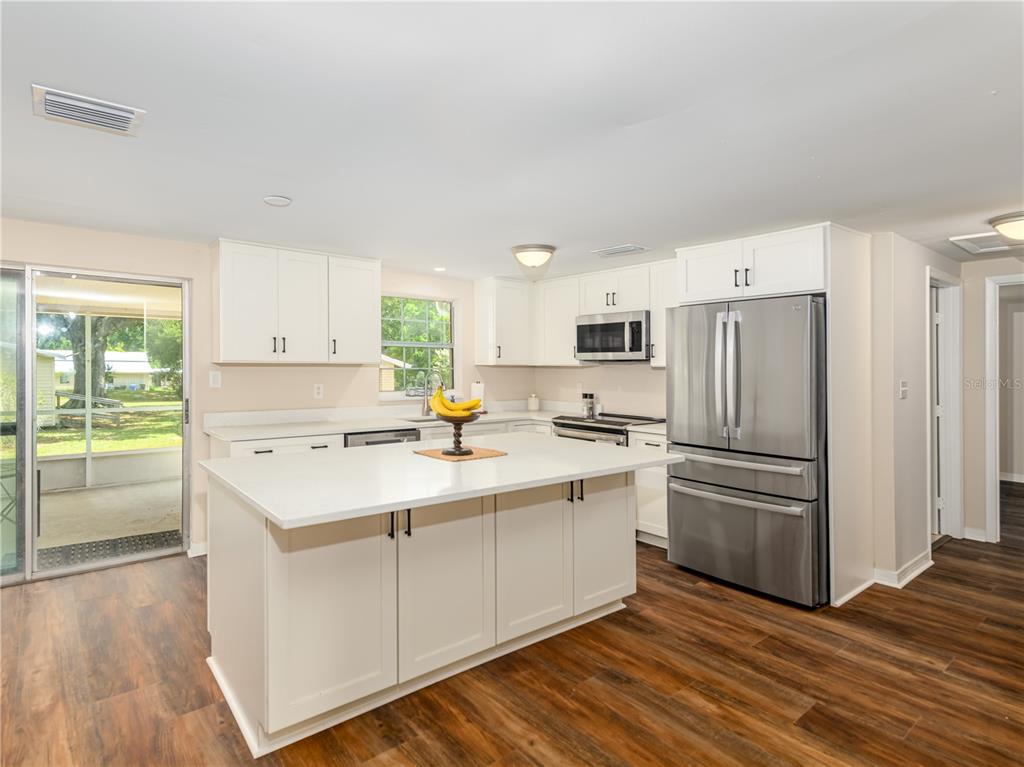 A kitchen features white cabinets, a central island with a white countertop, and stainless appliances — 4722 STEARNS ROAD, VALRICO, FL