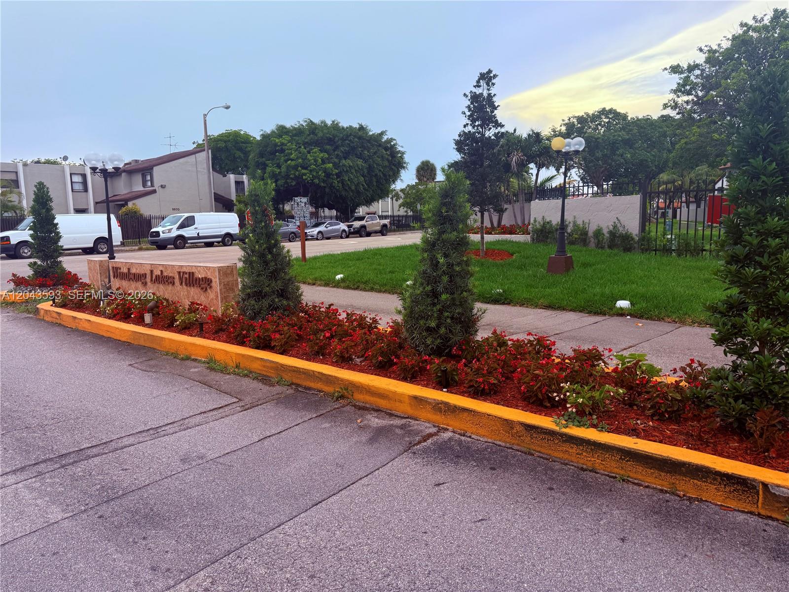 The entrance to Windsong Lakes Village features a stone sign, landscaping, and a paved driveway — 9909 NW 9th St Cir # 3, Miami FL 33172, MIAMI, FL