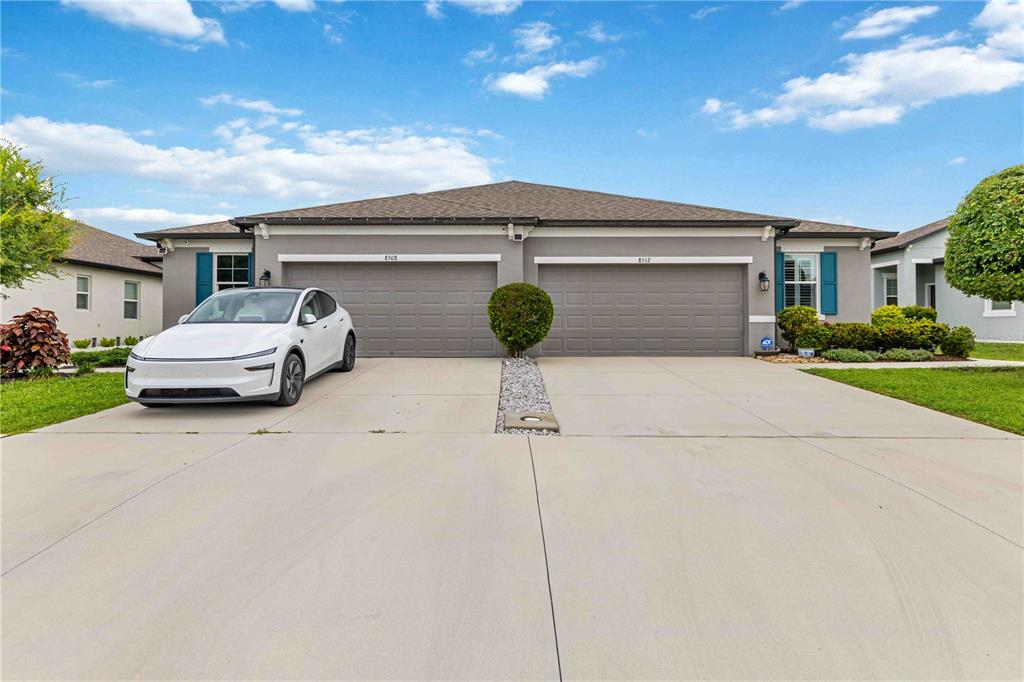 A duplex house features two garage doors, a white car, and a paved driveway — 8512 CACHE DRIVE, SARASOTA, FL