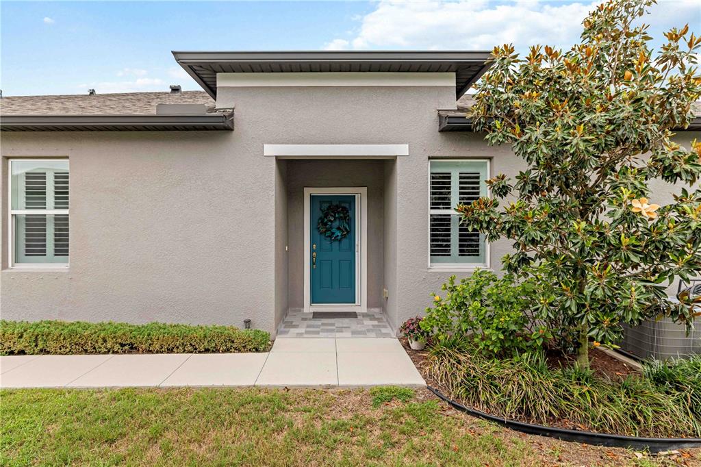A gray house exterior features a teal front door, two windows, and a landscaped yard — 8512 CACHE DRIVE, SARASOTA, FL