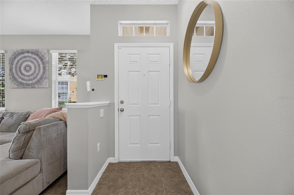 An entryway features a white front door, a gold oval mirror, and tile flooring — 8833 MOONLIT MEADOWS LOOP, RIVERVIEW, FL