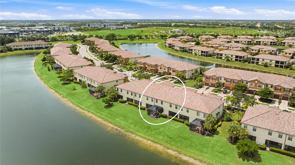 An aerial view shows a multi-story residential building with a screened patio by a lake — 20185 LAGENTE CIRCLE, VENICE, FL