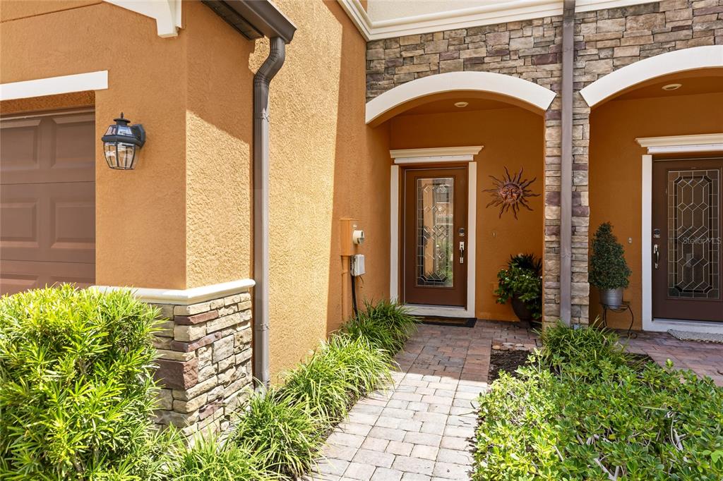 A paved walkway leads to the front entrances of a home with stucco and stone siding — 20185 LAGENTE CIRCLE, VENICE, FL