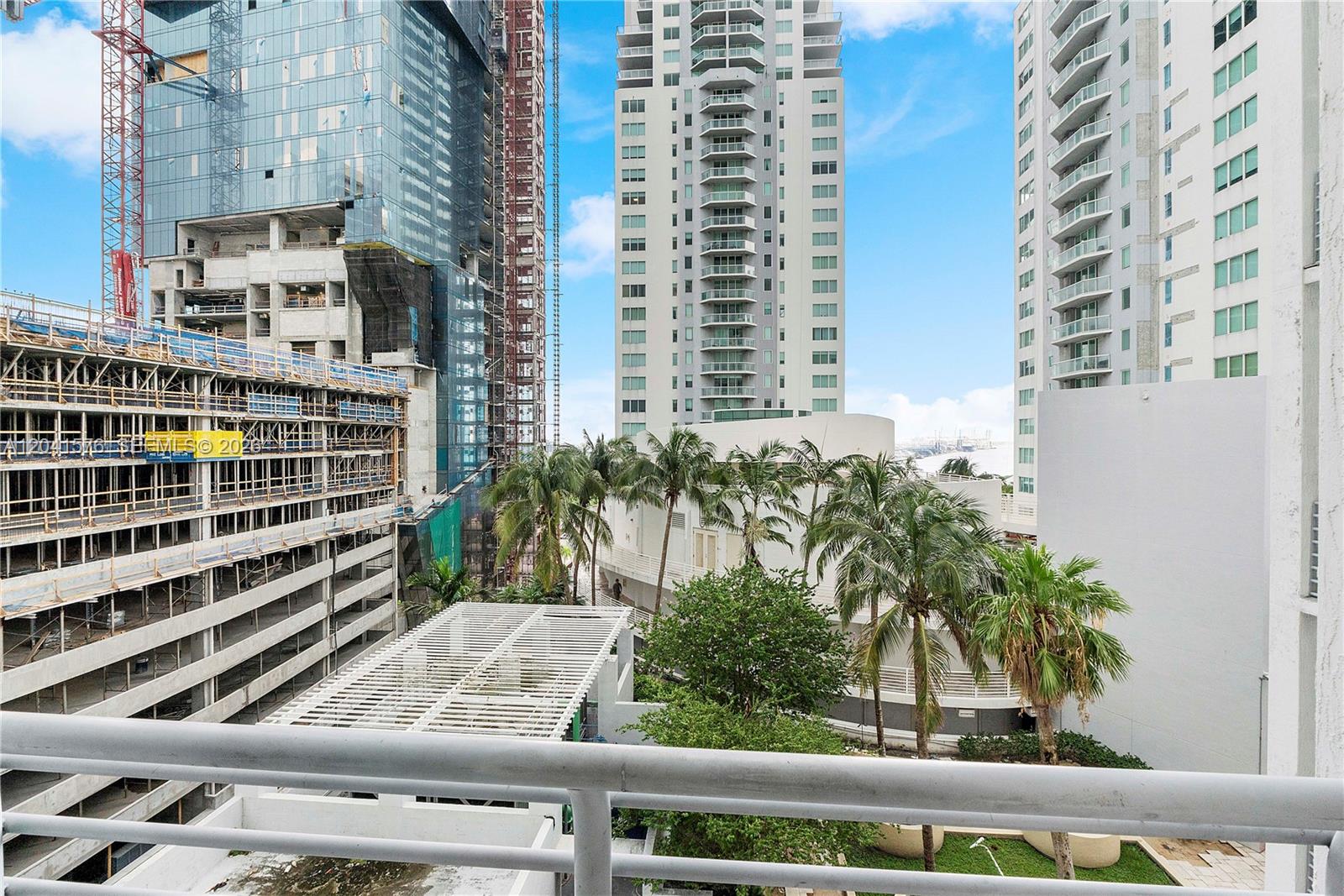 A view from a balcony overlooking a construction site, palm trees, and high-rise buildings — 234 NE 3rd St # 1404, Miami FL 33132, MIAMI, FL