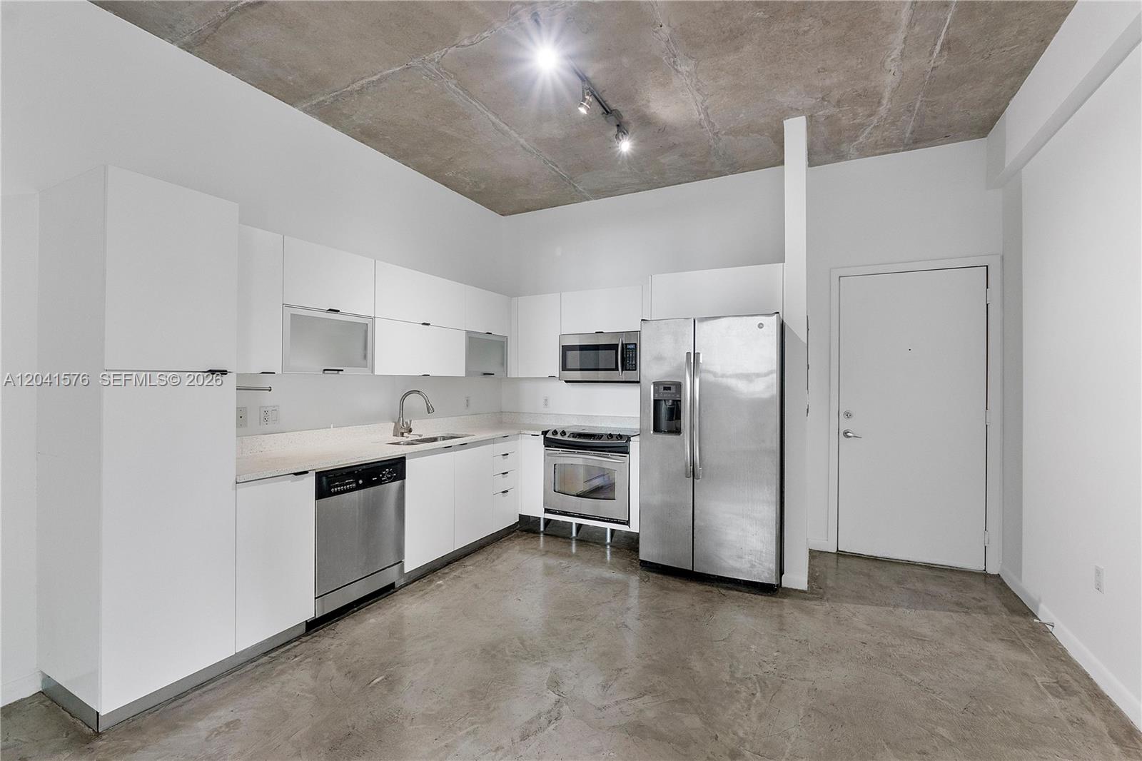 A modern kitchen features white cabinets, stainless steel appliances, and an exposed concrete ceiling — 234 NE 3rd St # 1404, Miami FL 33132, MIAMI, FL